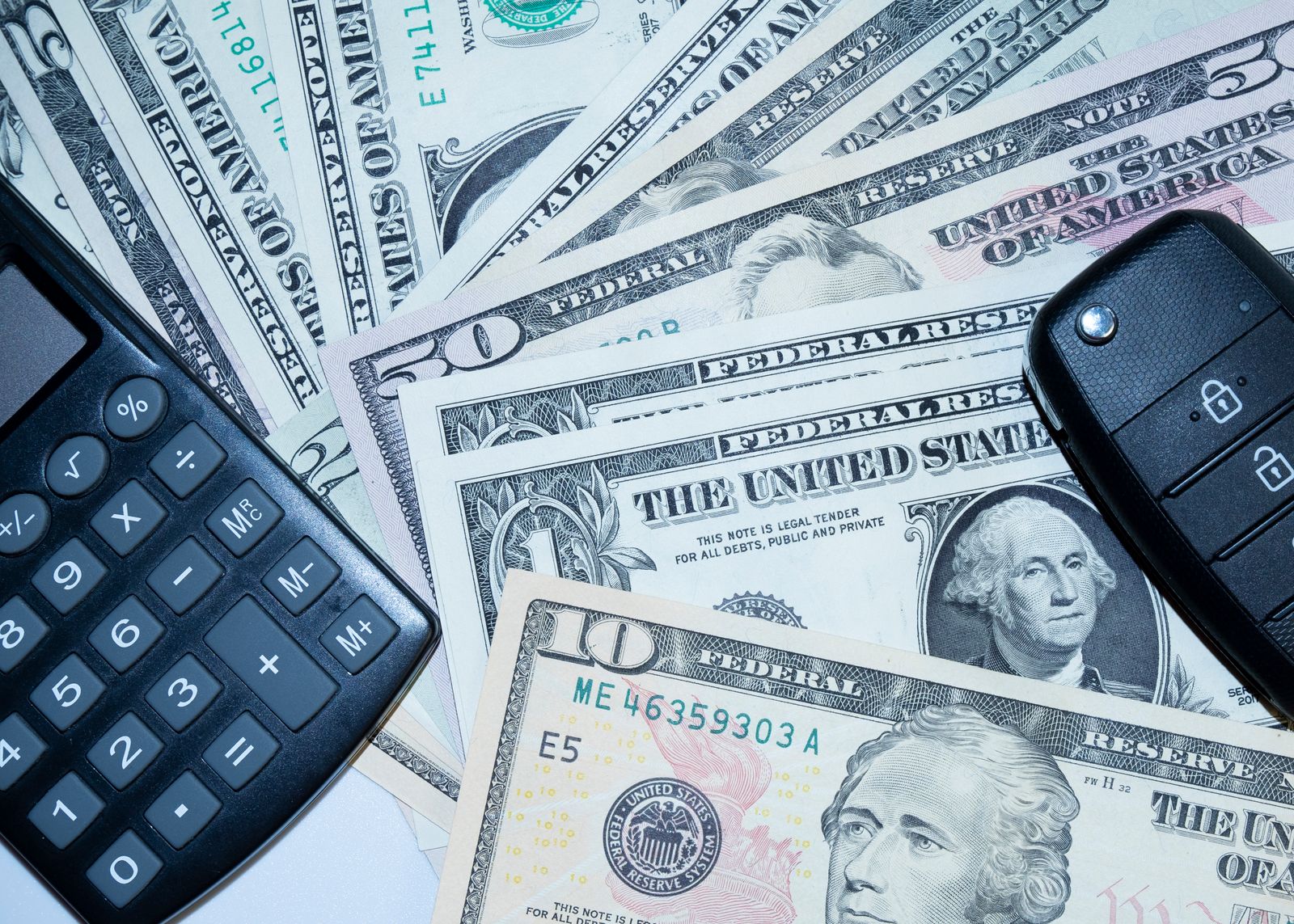 US dollar bills fanned out with a car key fob and a calculator resting on top.