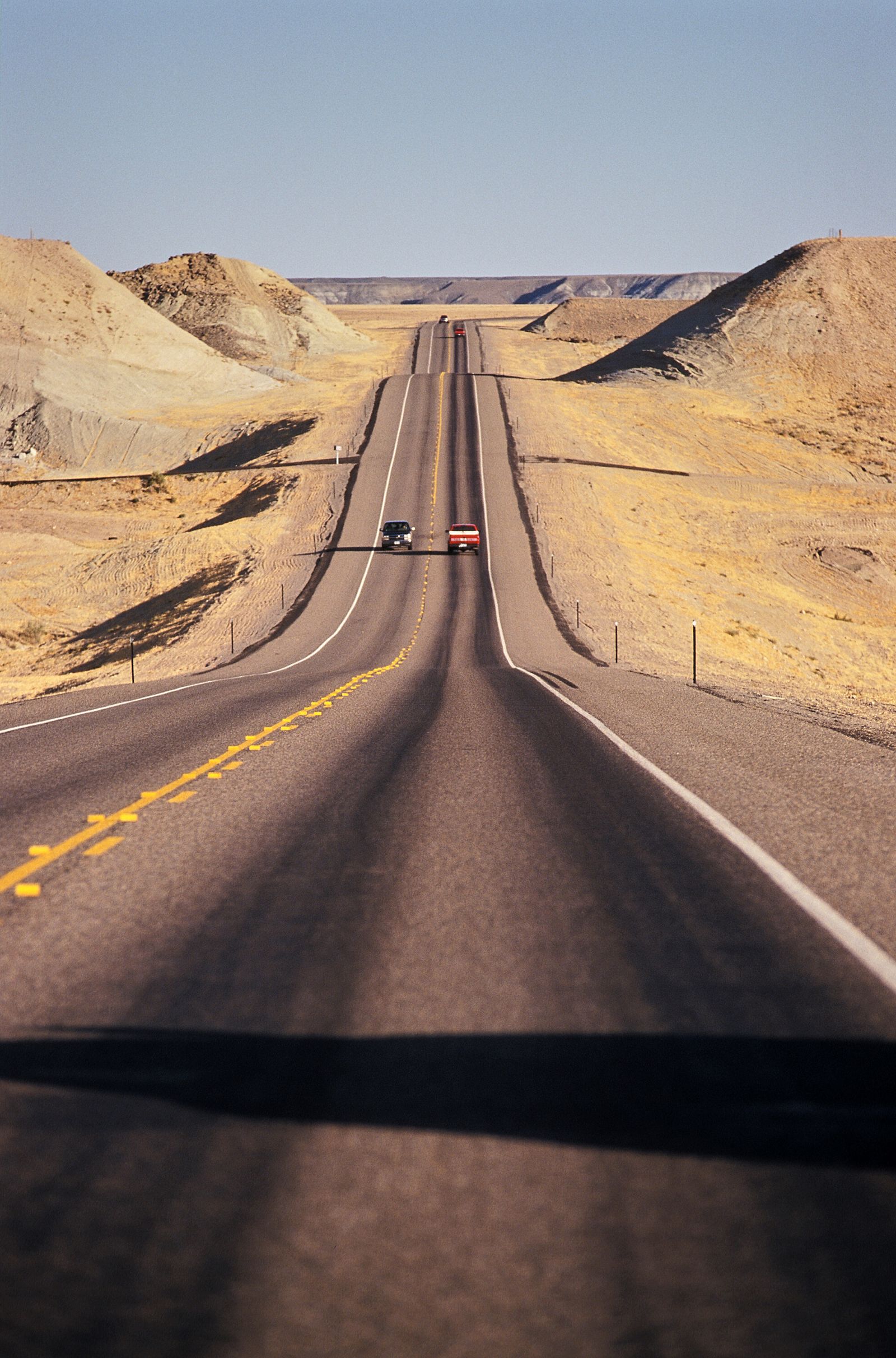 An empty highway with a double yellow line curving over rolling high-desert hills toward the horizon in Wyoming.