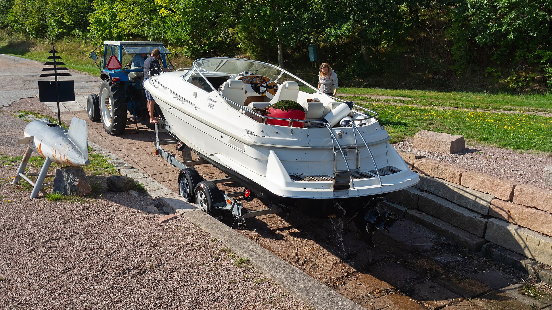 A white motorboat sitting on a road trailer at a slipway, hitched to a tractor and ready to be towed.