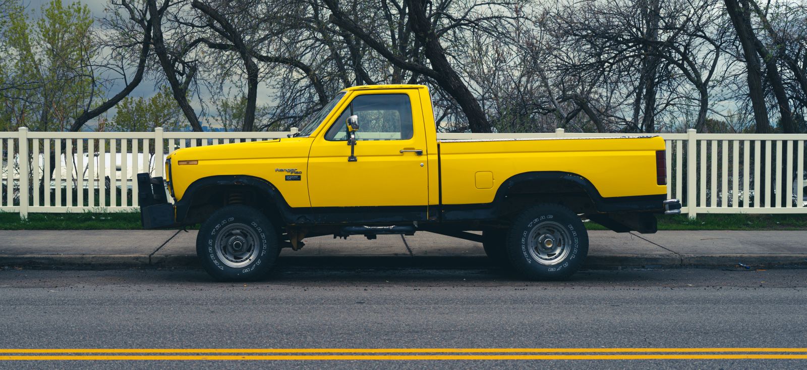 A yellow Ford pickup truck photographed side-on, parked at the kerb of a residential street.