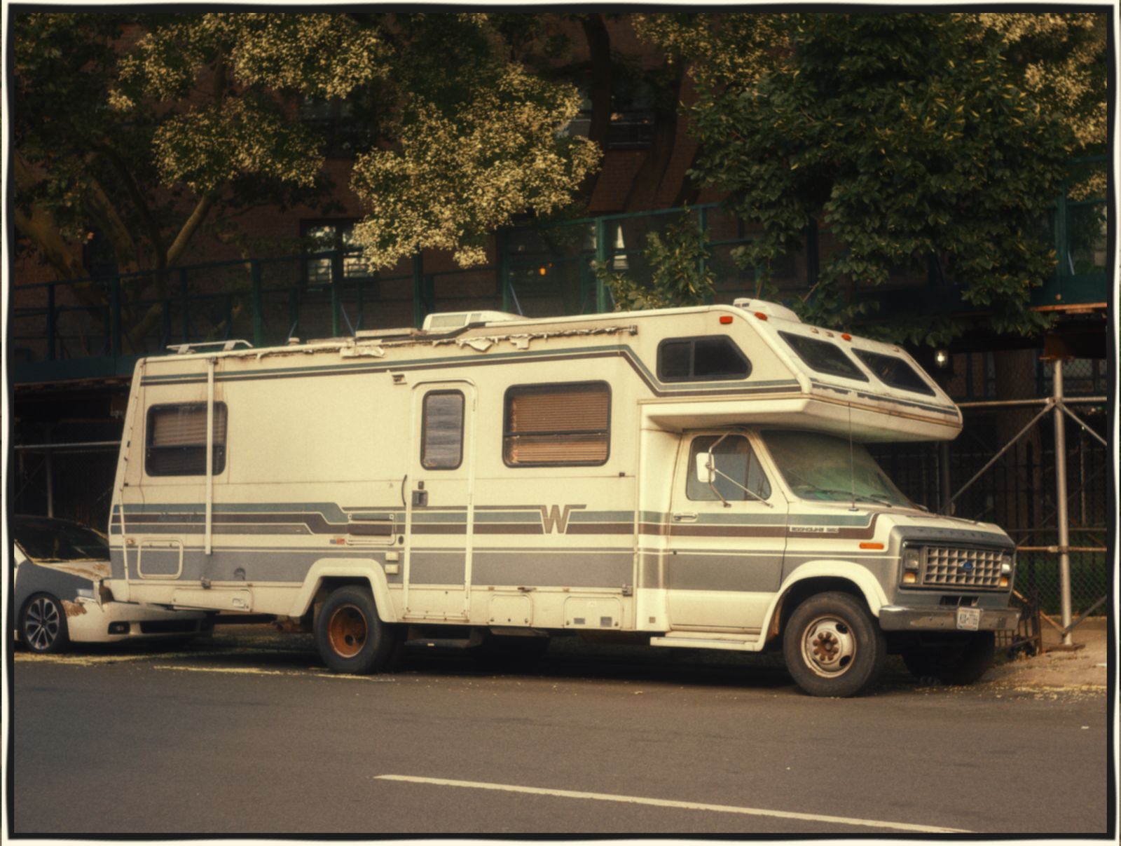 A cream Winnebago motorhome parked at the kerb on a tree-lined street.